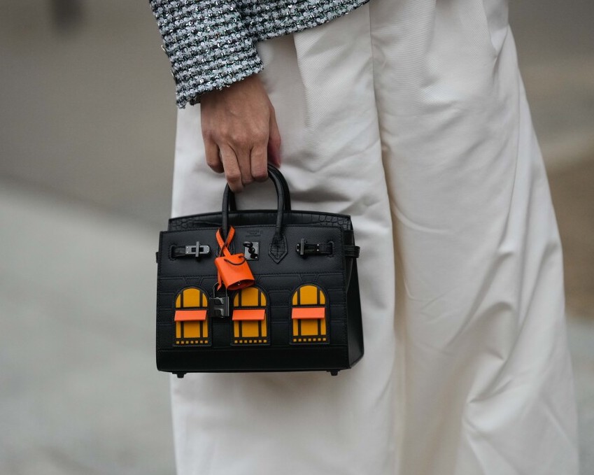 PARIS, FRANCE - JANUARY 25: A guest wears a silver embroidered sequined jacket, white wide legs pants, a black shiny leather and orange building pattern Birkin handbag from Hermes, outside Zuhair Murad, during Paris Fashion Week - Haute Couture Spring Summer, on January 25, 2023 in Paris, France. (Photo by Edward Berthelot/Getty Images)